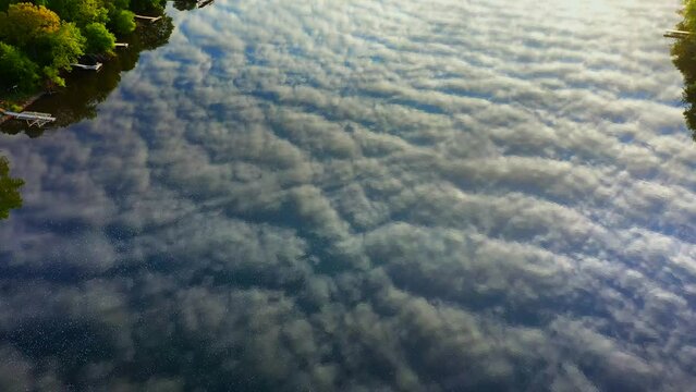 Amazing sky with rippled clouds, mirrored in tranquil river at daybreak, moving aerial view.

