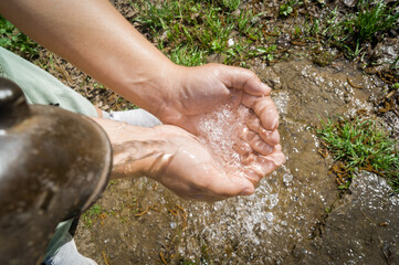 Cold water from a drinking column pours into the hands of a woman. Close-up. An urban street place...