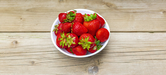 Top view of juicy strawberries in a wicker bowl on a rustic wooden table