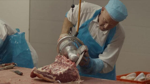 Butcher using electric saw to cut piece of meat