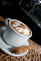 A cup of espresso cappuccino with a sprinkling of cinnamon powder. Additional sweet bread cake background and cinnamon sticks.