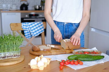 Healthy farm fresh food on the kitchen table. Fresh homemade bread. Cooking sandwiches at home. Hearty snack or breakfast. Simple whole food in rustic style. In the background, a woman is cooking.