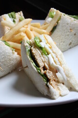 Triangular shaped sandwich. Stuffed thick meat, thin cheese, mayonnaise, lettuce. Pierced with a toothpick. On a white ceramic plate. close up.