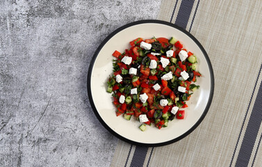 Greek salad with cucumbers, tomatoes, onions, olives, feta cheese and herbs on a round plate on a dark gray background. Top view, flat lay