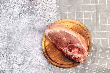 Raw pork shoulder on the skin with bone on a round wooden cutting board on a dark grey background. Top view, flat lay