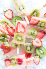 Several refreshing strawberry kiwi popsicles in a pile on ice.