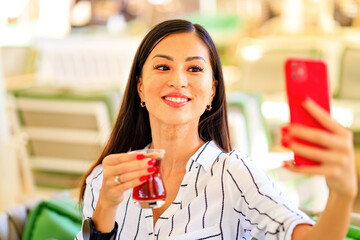 Portrait of successful business asian women in striped shirt outdoor drinking a turkish tea and taking selfie