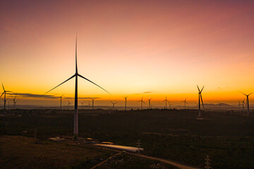 Wind turbine farm in a big green field generating electricity at sunset. Clean alternative energy concept to reduce global warming and climate change for sustainable growth and development.