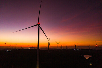 Fototapeta na wymiar Wind turbine farm in a big green field generating electricity at sunset. Clean alternative energy concept to reduce global warming and climate change for sustainable growth and development.