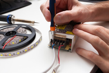 LED strip on the coil is connected to a voltage converter. Hands of the master in the frame.