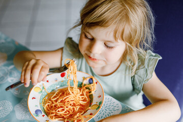 Adorable toddler girl eat pasta spaghetti with tomato bolognese with minced meat. Happy preschool...