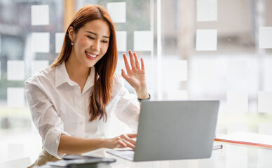 Happy young asian business woman waving hands to greeting partner during making video conference...