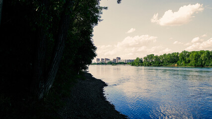 Irtysh river with green trees on the banks. Green forest. River landscape. Apartment buildings....