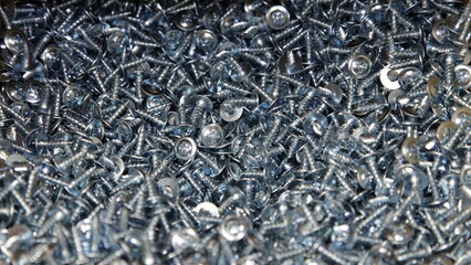 New short gray self tappers screws with cross heads. Zinc galvanized construction fasteners. Industrial texture for the background.
