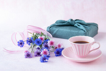 コーヒーとヤグルマギクの花束と風呂敷包みのデザイン（ペールピンクの背景）	
