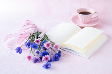 ピンクのカップのコーヒーとヤグルマギクの花束と見開きの本（ペールピンクの背景）