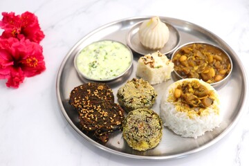 Indian vegetarian lunch or dinner Thali includes beans sabzi, dal rice, Alu Vadi, dhokla, veg cutlet, raita, and ukdiche modak.  Indian food is served on a plate or thali. Ganesh Jayanti Food. Copy