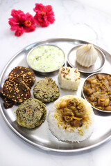 Indian vegetarian lunch or dinner Thali includes beans sabzi, dal rice, Alu Vadi, dhokla, veg cutlet, raita, and ukdiche modak.  Indian food is served on a plate or thali. Ganesh Jayanti Food. Copy