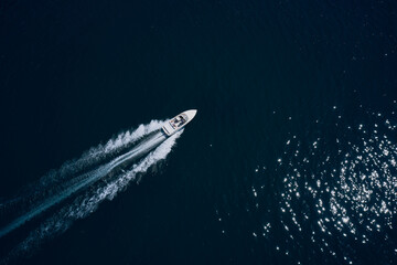 Top view of a white boat sailing to the blue sea. Drone view of a boat sailing.Motor boat in the sea. Travel - image. Large white boat fast movement on blue water aerial view.