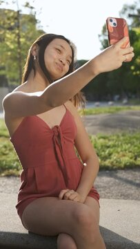 Young Asian woman waving hand and posing while taking selfies or having a video call on her mobile phone. Vertical video