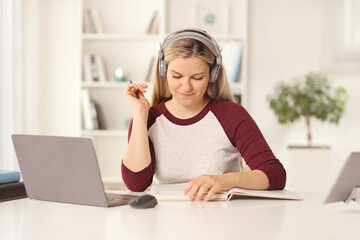 Young female student sitting in front of a laptop computer at home with headphones