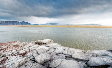 The shore of the Krasnoyarsk reservoir, gray sandstone and stones with slabs on the shore, rainy sky over Mount Tepsey Tepsei