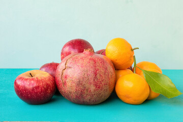 Naklejka na ściany i meble Pomegranates, apples, and tangerines on a turquoise background. Ripe fruits.