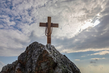 Crucifix symbol and beads on top rock mountain with bright sunbeam on the colorful sky background
