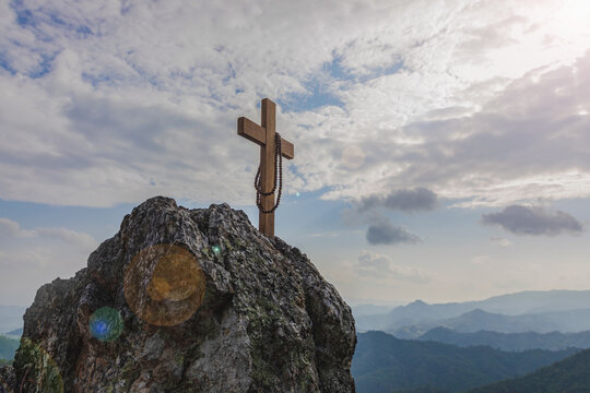 Christian cross and rosary on top rock mountain with bright sunbeam on the colorful sky background