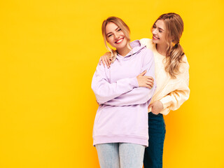 Two young beautiful smiling blond hipster female in trendy summer clothes. Sexy carefree women posing near yellow wall in studio. Positive models having fun. Cheerful and happy
