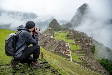 Papier Peint photo Machu Picchu Asian man tourist and photographer taking photo at Machu Picchu, one of seven wonders and famous tourist attraction in Cusco Region of Peru. This majestic place has known as Lost City of the Incas.