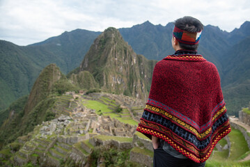 Asian man tourist in traditional Peruvian clothing looking at Machu Picchu, A famous tourist...