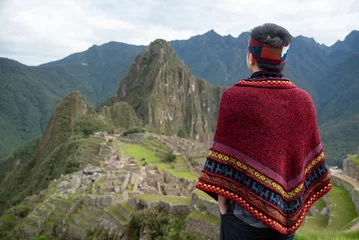Papier Peint photo Machu Picchu Asian man tourist in traditional Peruvian clothing looking at Machu Picchu, A famous tourist attraction in Cusco Region of Peru. This majestic place has known as Lost City of the Incas.