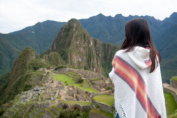 Asian woman tourist in traditional Peruvian clothing looking at Machu Picchu, A famous tourist attraction in Cusco Region of Peru. This majestic place has known as Lost City of the Incas.