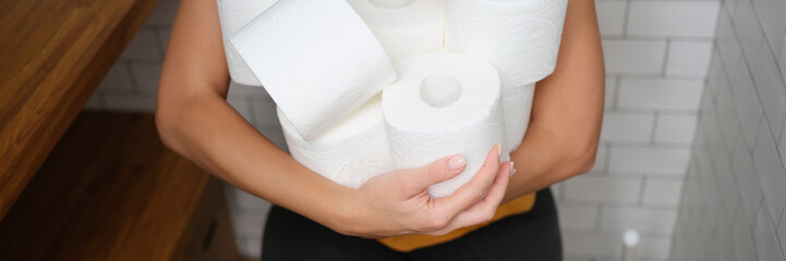 Woman sitting on toilet with rolls of toilet paper
