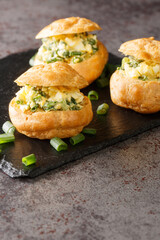 Profiteroles stuffed with egg salad with green onions close-up on a slate board on the table. vertical