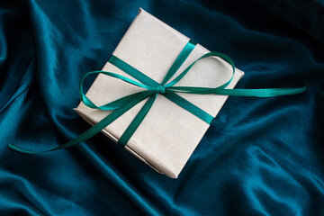 Gift box wrapped in craft paper with emerald green satin ribbon. Happy New Year. Birthday present on silk emerald green background