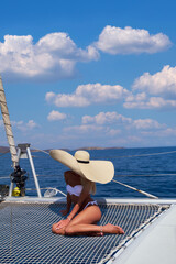 Beautiful young blond woman in bikini sitting on catamaran at sunny summer day