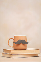 Brown mug of coffee with a mustache and a book. Happy father's day concept. vertical photo