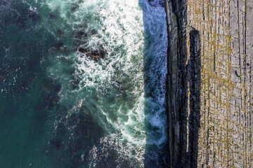 Ocean waves hit cliffs. Rough stone coastline of Aran island, county Galway, Ireland. Aerial top down view. Irish nature landscape.