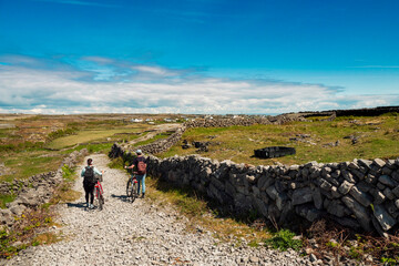 Couple pushing bikes on a rough small road. Aran island, county Galway, Ireland. Warm sunny day....
