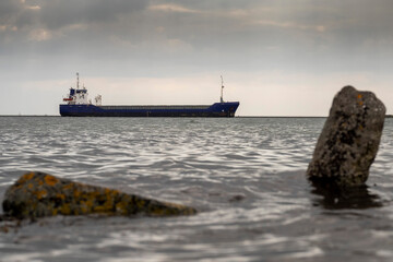 Cargo ship in focus. Rough stone rocks in foreground out of focus. Danger of the ocean. World goods...