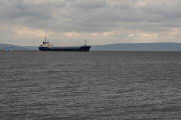 Side view of a cargo ship in the ocean. Dark and moody image with cloudy sky and calm water surface. International shipment and import and export industry. Goods delivery by ocean.