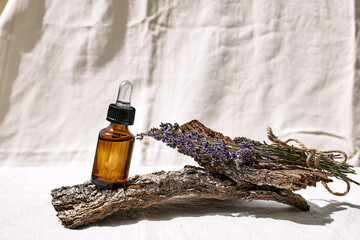 Dropper bottle with natural essential lavender oil and lavender flower on wooden bark as podium on...