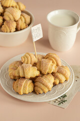 Pastry rolls. Mini cottage cheese croissants. Bagels with sugar on the milky color ceramic plate. Mug with milk, ceramic bowl with pastry rolls, vintage paper pictures 