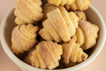 Pastry rolls. Mini cottage cheese croissants, close up. Bagels with sugar in the ceramic bowl. Dusty rose background