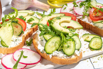 Toast with cream cheese or cottage cheese, with fresh vegetables - tomato, avocado, radish, cucumber, healthy diet spring sandwiches, Scandinavian toasts top view copy space