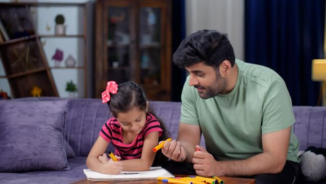 A caring Indian father helping his little daughter in completing her holiday homework - father-daughter bonding  leisure time. A cute little girl child - modern-day father  parenting  girl child ed...