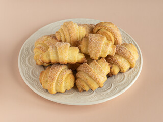 Pastry rolls. Mini cottage cheese croissants. Bagels with sugar on the milky color ceramic plate. Dusty rose background