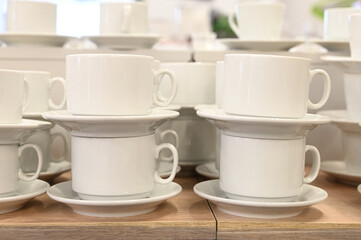 Pairs of mugs and plates on shelf of the tableware store. A lot of rows of pure white cups with plates for coffee break